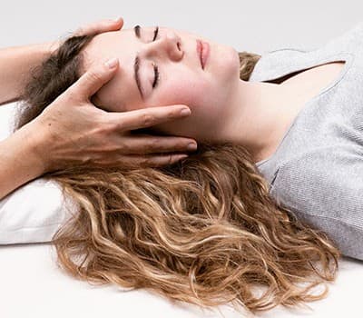 Craniosacraltherapie in der Praxis – sanfte, gehaltene Berührung am Kopf einer entspannten Klientin